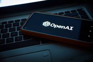 An image of a phone placed on a laptop. The phone has the OpenAI logo on screen. The company behind ChatGPT have entered into a deal with Axel Springer